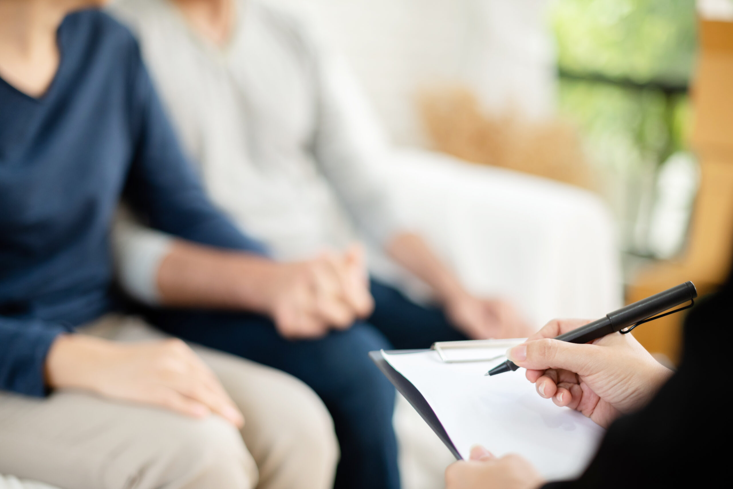 Young man and woman consulting with professional consultant. Couple sitting on sofa and holding hands together.